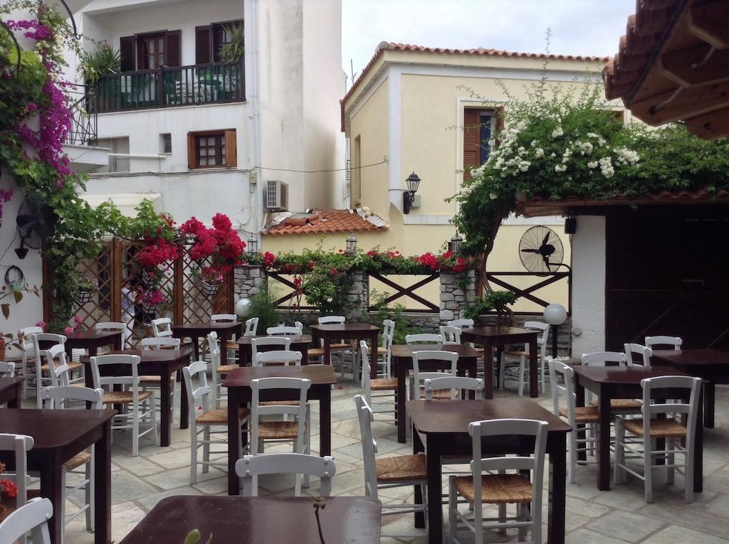 Un café en plein air, avec des tables et des chaises, entouré de bâtiments et de plantes en fleurs.