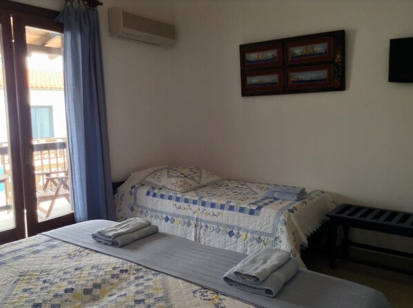 A bedroom with two beds, a window with curtains, a wall-mounted picture, and a small table. - Mouria (Skiathos)