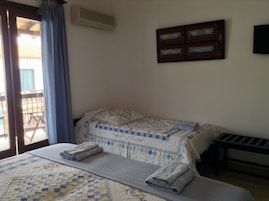 Un dormitorio con dos camas, una ventana con cortinas, un cuadro en la pared y una mesita.
