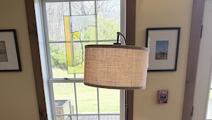 A dining area with a table covered by a floral tablecloth, a puzzle box, chairs, a hanging lamp, and a window with a view of the outdoors. - The Old Lantern Inn and Barn (Charlotte)