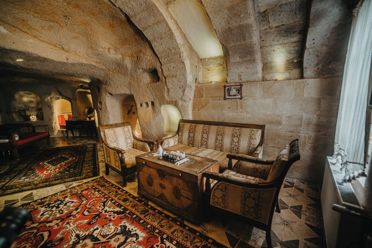 A room with a stone ceiling, a sofa set, a wooden chest, and a patterned rug.