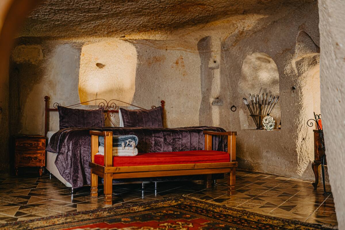 A rustic bedroom with a wooden bed, a patterned rug, and a stone wall.