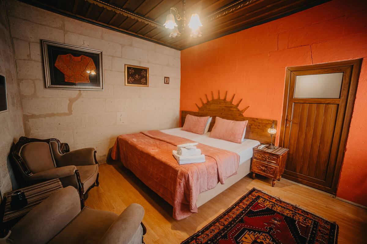 A bedroom with a bed, a chair, a nightstand, a wooden door, and a wall with a picture frame.