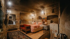 A rustic room with a bed, a wooden chair, a small table with a kettle, and a cabinet. - Helios Cave Hotel (Ürgüp)