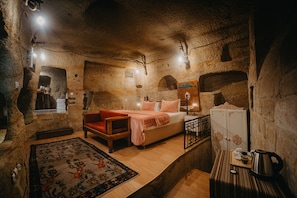 A rustic room with a bed, a wooden chair, a small table with a kettle, and a cabinet. - Helios Cave Hotel (Ürgüp)
