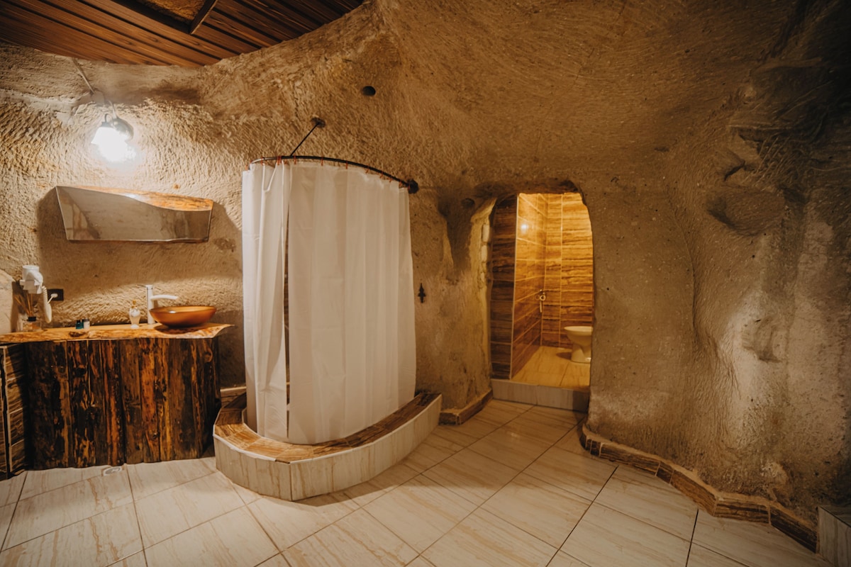 Un baño rústico con tocador de madera, cortina de ducha blanca y pared de piedra.