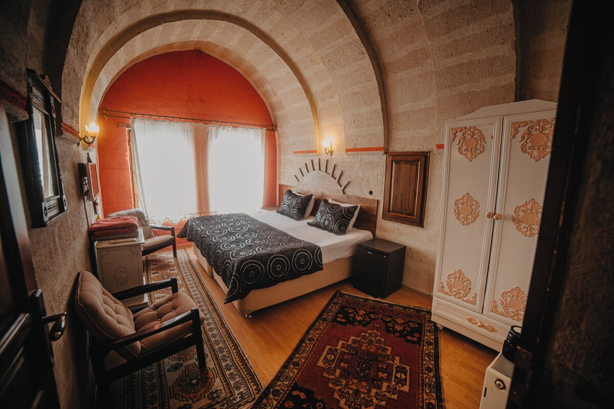 A bedroom with an arched ceiling, a bed with patterned bedding, a chair, a wardrobe, and a rug.