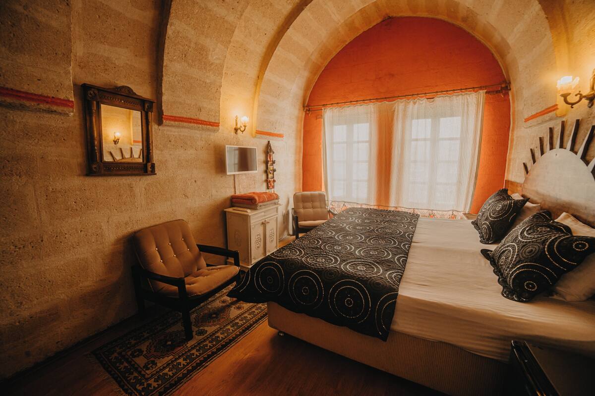 A room with a bed, a chair, a television, and a window with curtains.