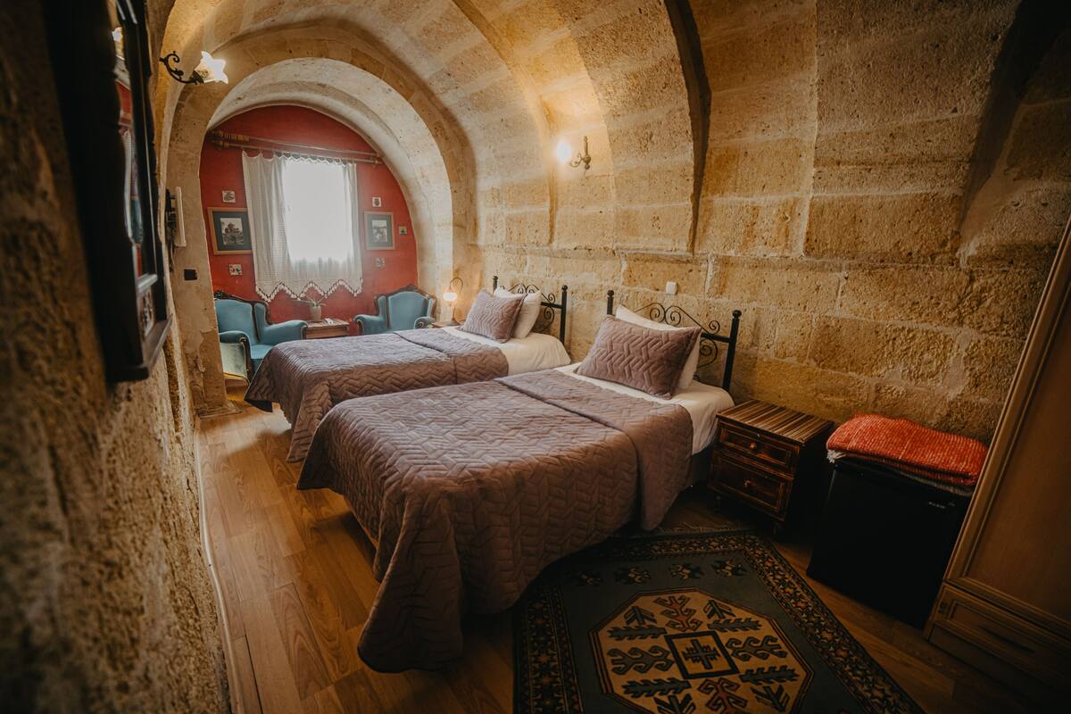 A room with two beds, a small table, a chair, and a decorative rug.