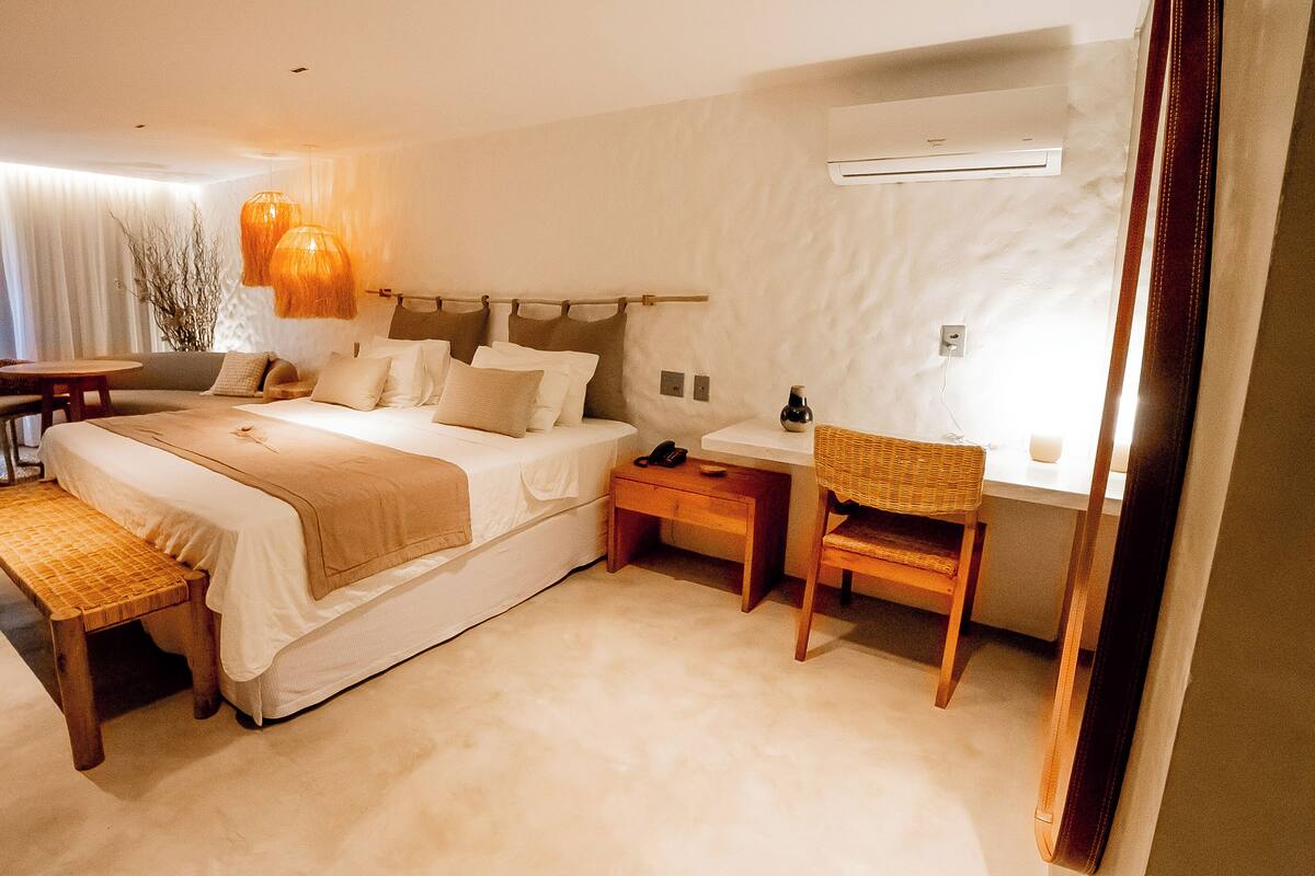 A bedroom with a large bed, bedside tables, a chair, an air conditioning unit, and a window.