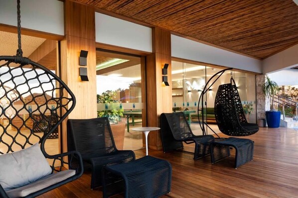 Un espacio interior moderno con mobiliario de mimbre, suelo de madera y puertas de cristal que dan a un área exterior.