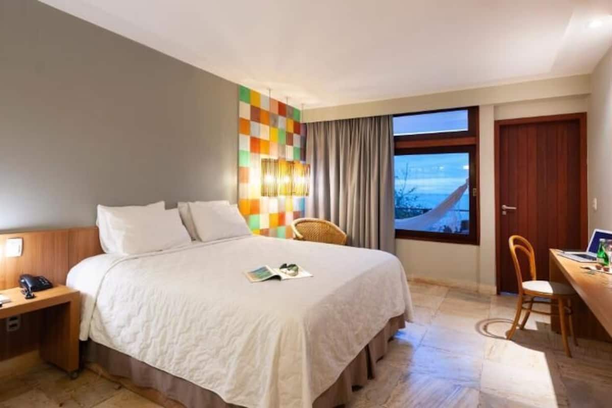 A hotel room with a bed, bedside table, desk, chair, and a TV.
