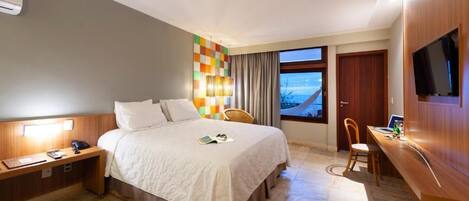 A hotel room with a bed, bedside table, desk, chair, and a TV.