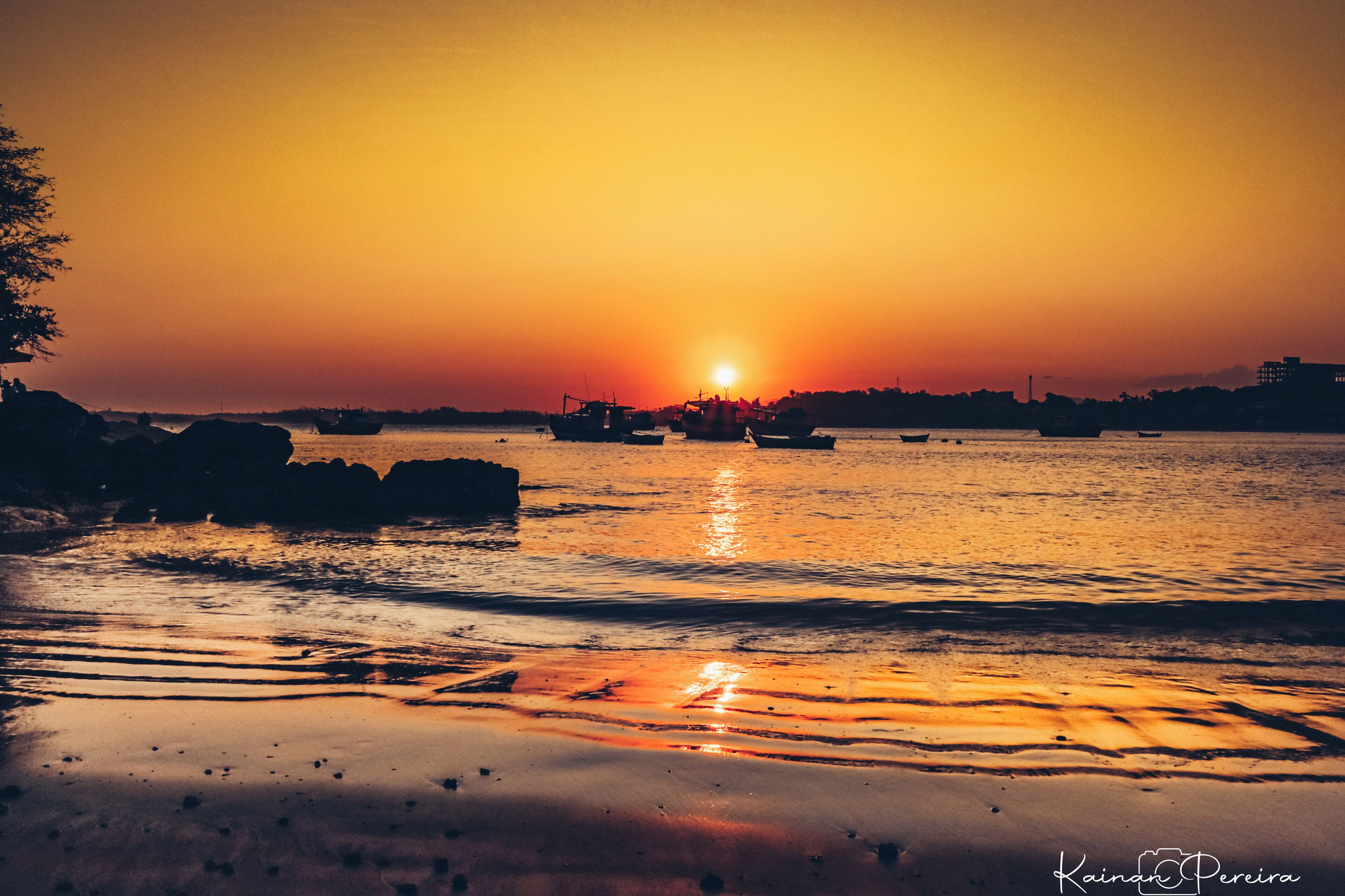 A sunset over a calm body of water with boats and rocky outcrops.