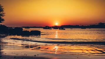 A sunset over a calm body of water with boats and rocky outcrops.