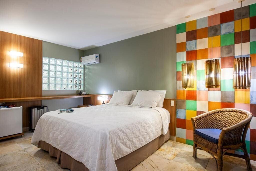 A hotel room with a large bed, a wooden nightstand, a wicker chair, and a colorful wall.