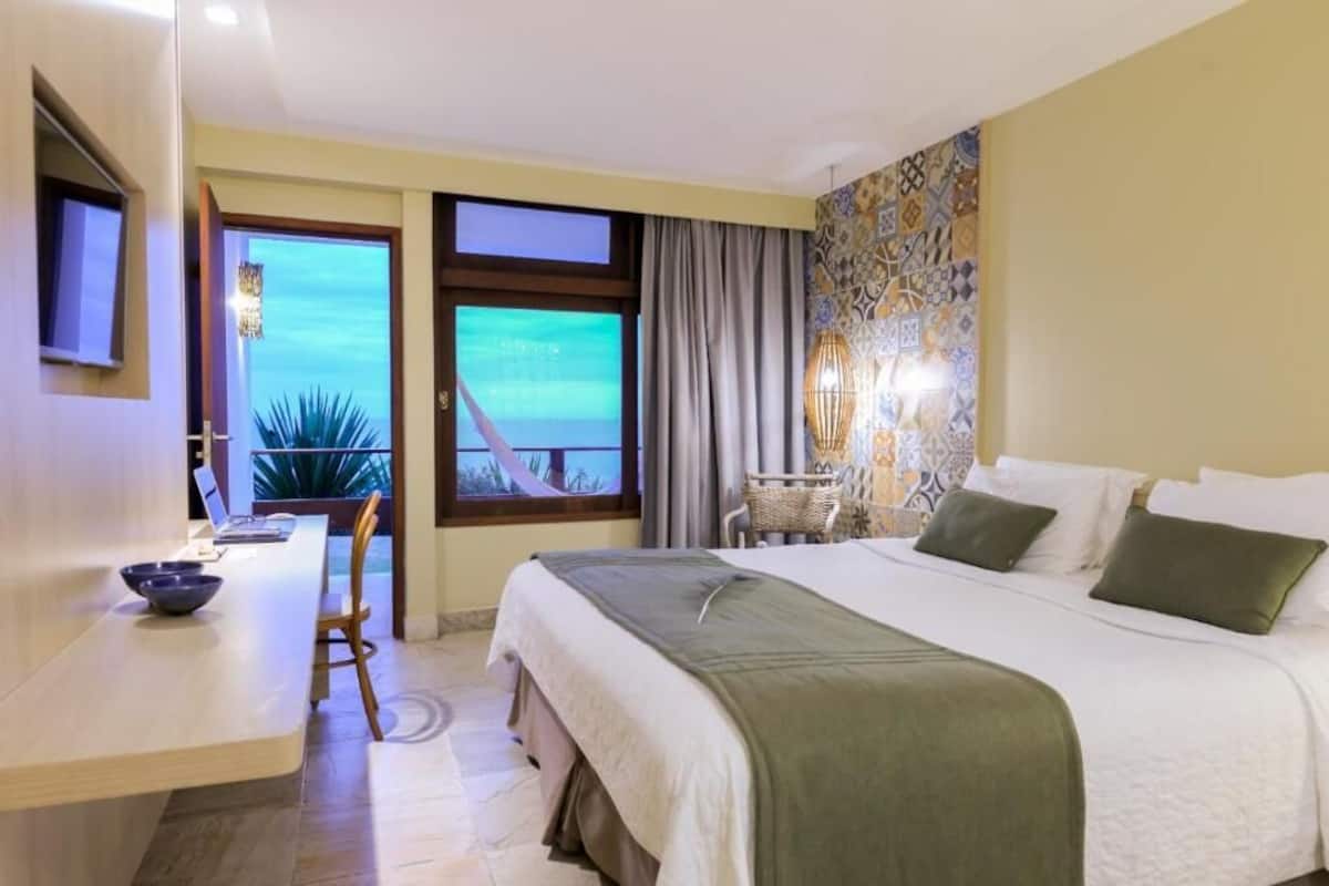A hotel room with a bed, a desk, a chair, a view of the ocean, and a patterned wall.
