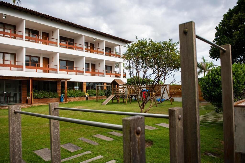 A multi-story building with a white exterior and brown balconies, a playground with a slide, and a well-maintained lawn.