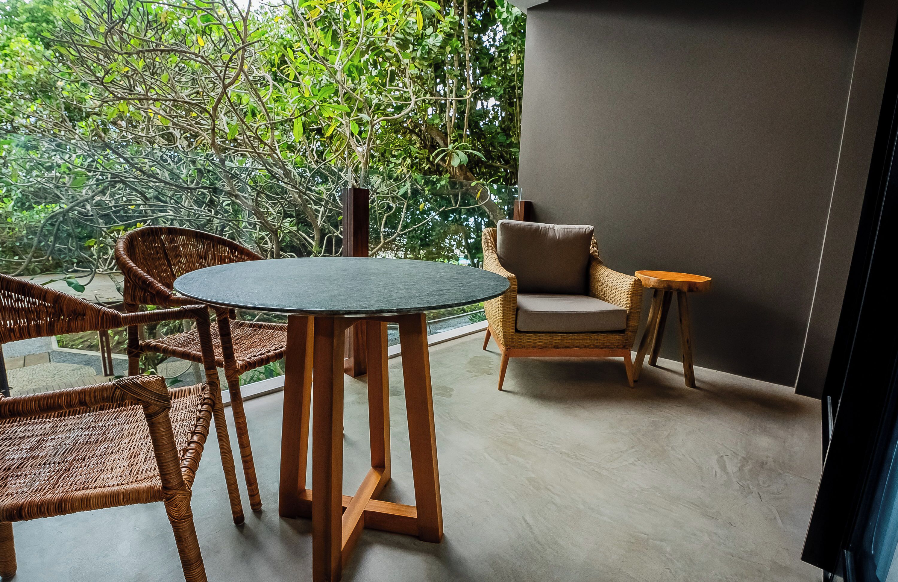 A balcony with wicker furniture, a round table, and a view of lush greenery.