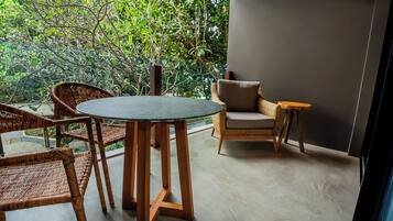A balcony with wicker furniture, a round table, and a view of lush greenery.