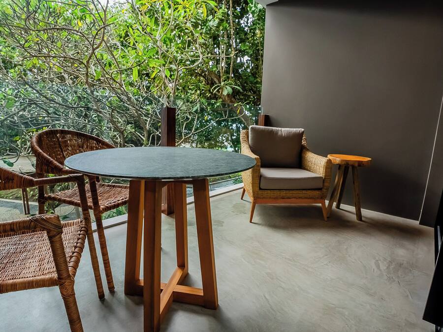 A balcony with wicker furniture, a round table, and a view of lush greenery.