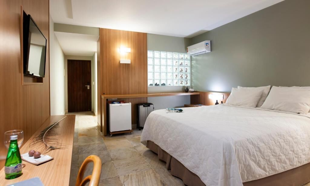 A hotel room with a bed, a desk, a chair, a mirror, a window with a view of shoes, and a radiator.