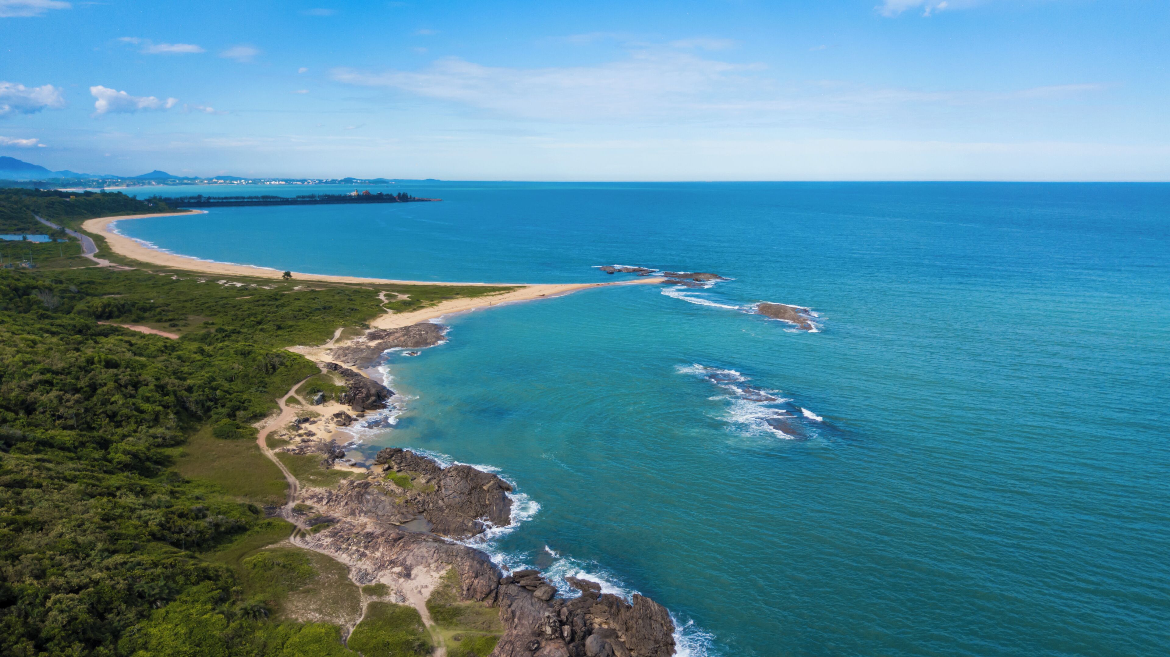 An aerial view of a coastal area with a beach, rocky shoreline, and surrounding greenery.