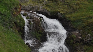 Una cascada fluye sobre rocas en un paisaje cubierto de hierba.