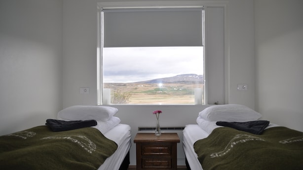 Una habitación con dos camas, una mesita de noche de madera y un ventanal con vistas al paisaje.