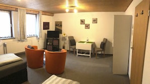 A compact room with a bed, two orange ottomans, a small table, and a TV. - Messezimmer4u (Düsseldorf)