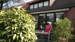A two-story house with a patio area featuring a table and chairs, surrounded by greenery. - Messezimmer4u (Düsseldorf)