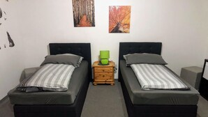 A room with two single beds, a small wooden nightstand with a green lamp, and two framed pictures on the wall. - Messezimmer4u (Düsseldorf)