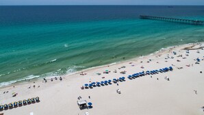 A beach with rows of umbrellas and sun loungers, a pier extending into the water, and clear skies.