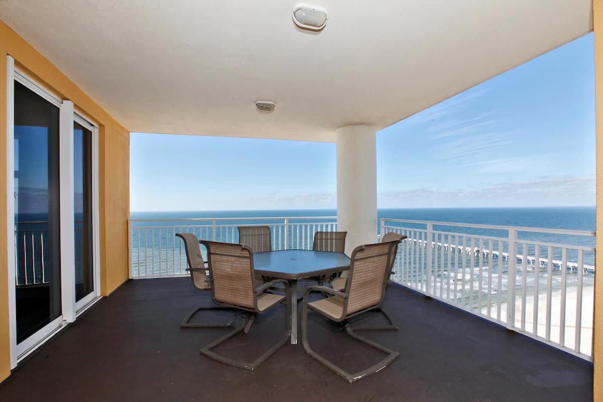 A balcony with a round table and four chairs, overlooking a beach and the ocean.