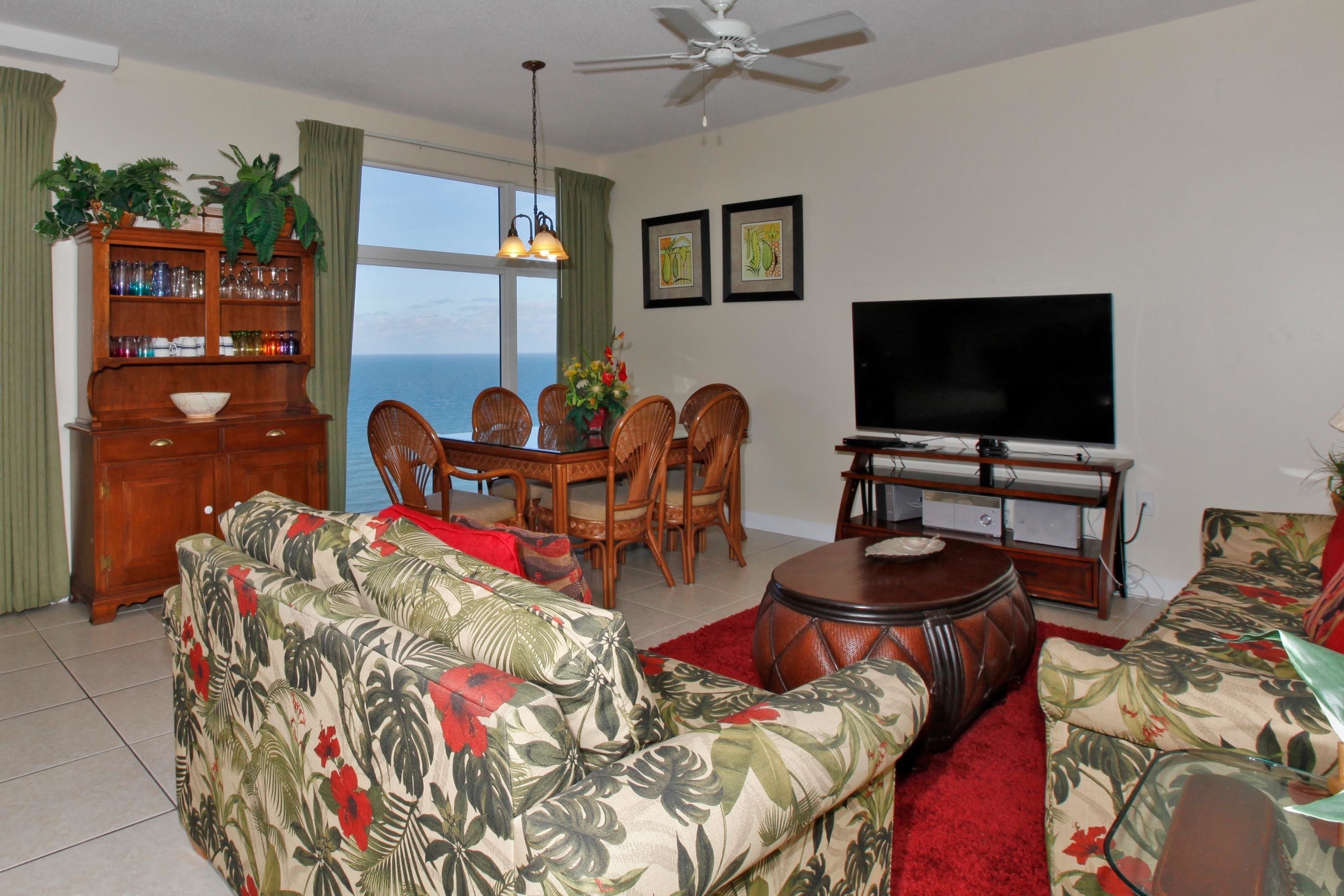 A living room with a sofa, a dining table with chairs, a television, and a ceiling fan.