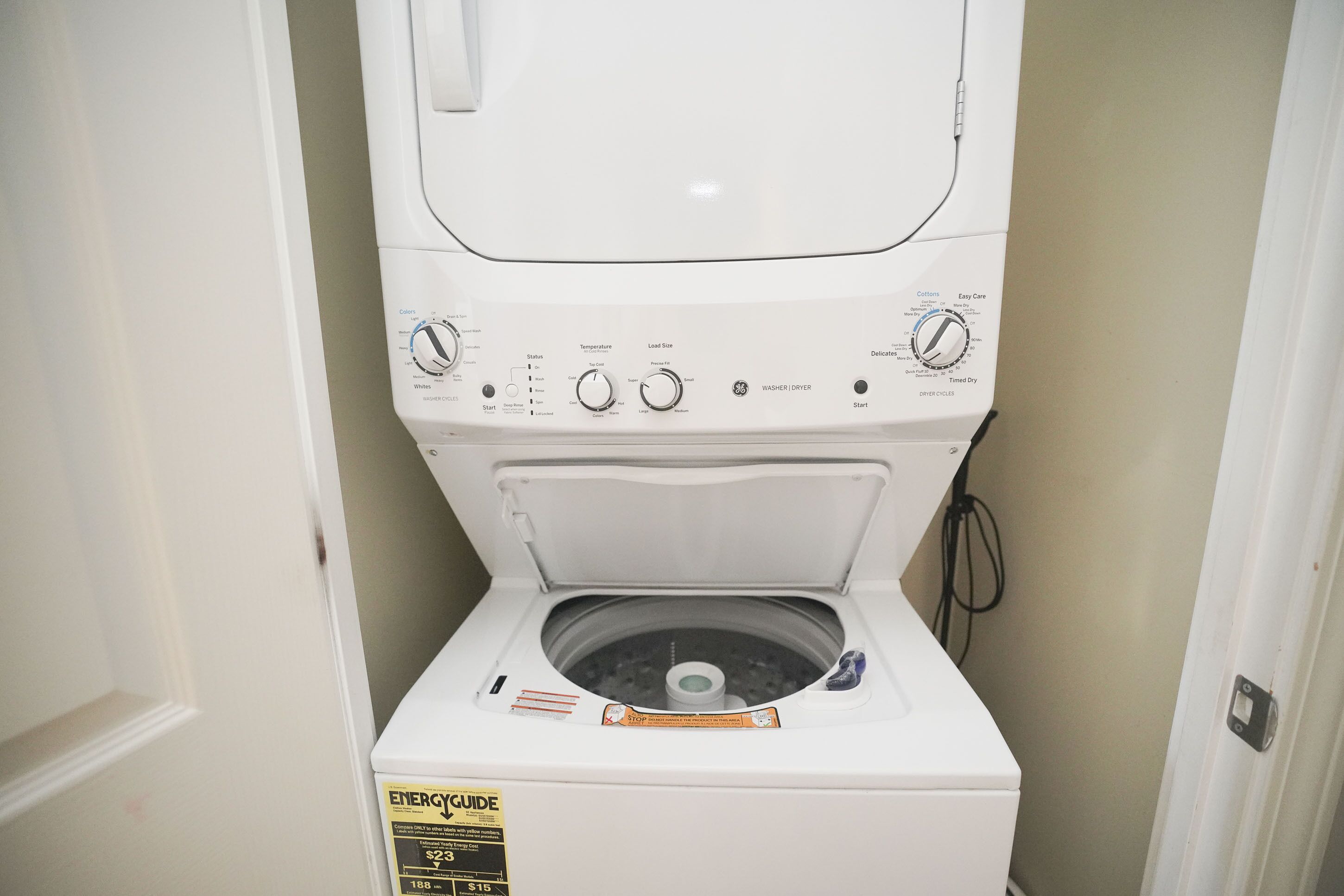 A front view of a white front-loading washing machine with a control panel, a front-loading door, and a label indicating ENERGY GUIDE information.