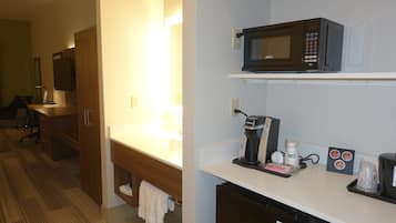 A hotel room with a kitchenette, including a microwave, coffee maker, and a small refrigerator.