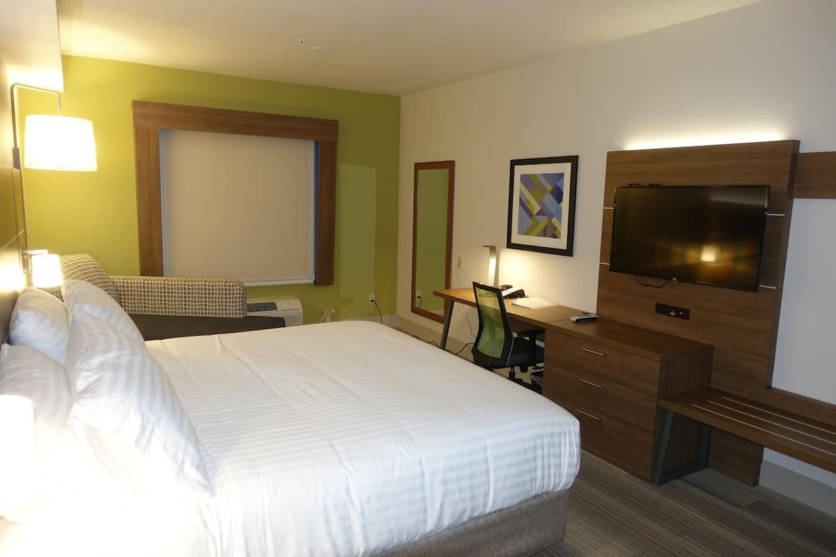 A hotel room with a large bed, a desk with a chair, a television, and a window with blinds.