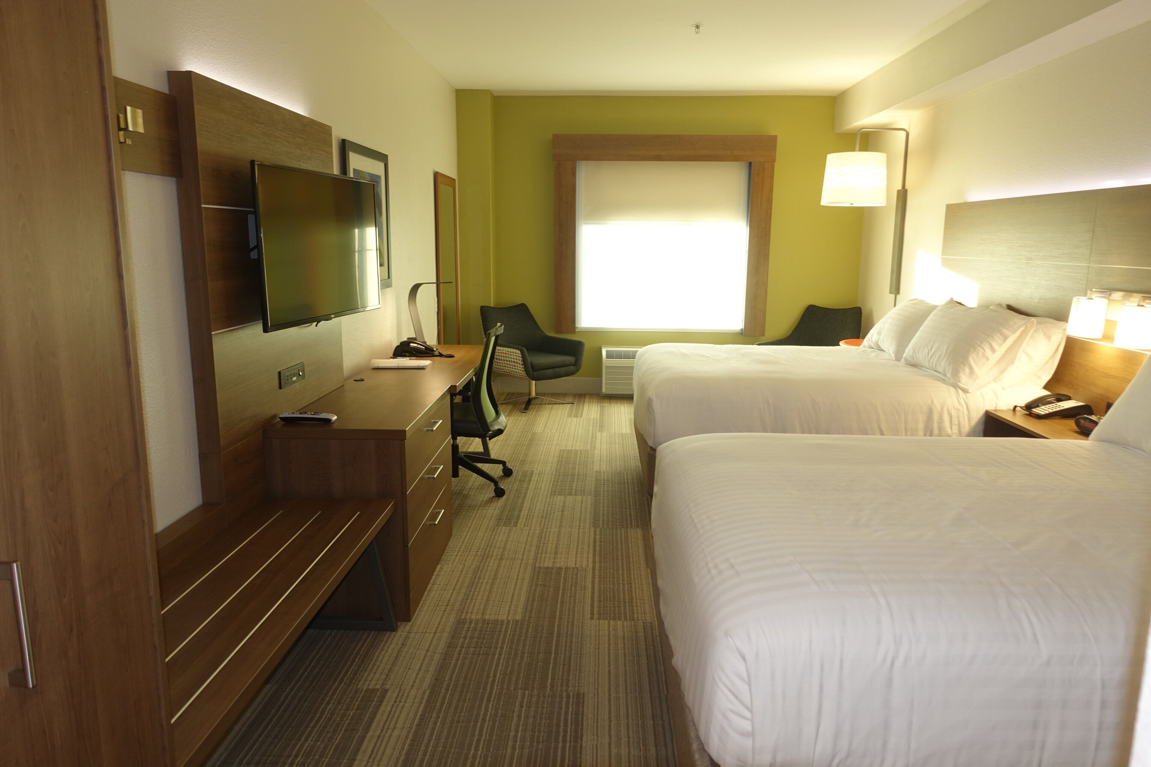 A hotel room with two beds, a desk, a chair, a TV, and a window.