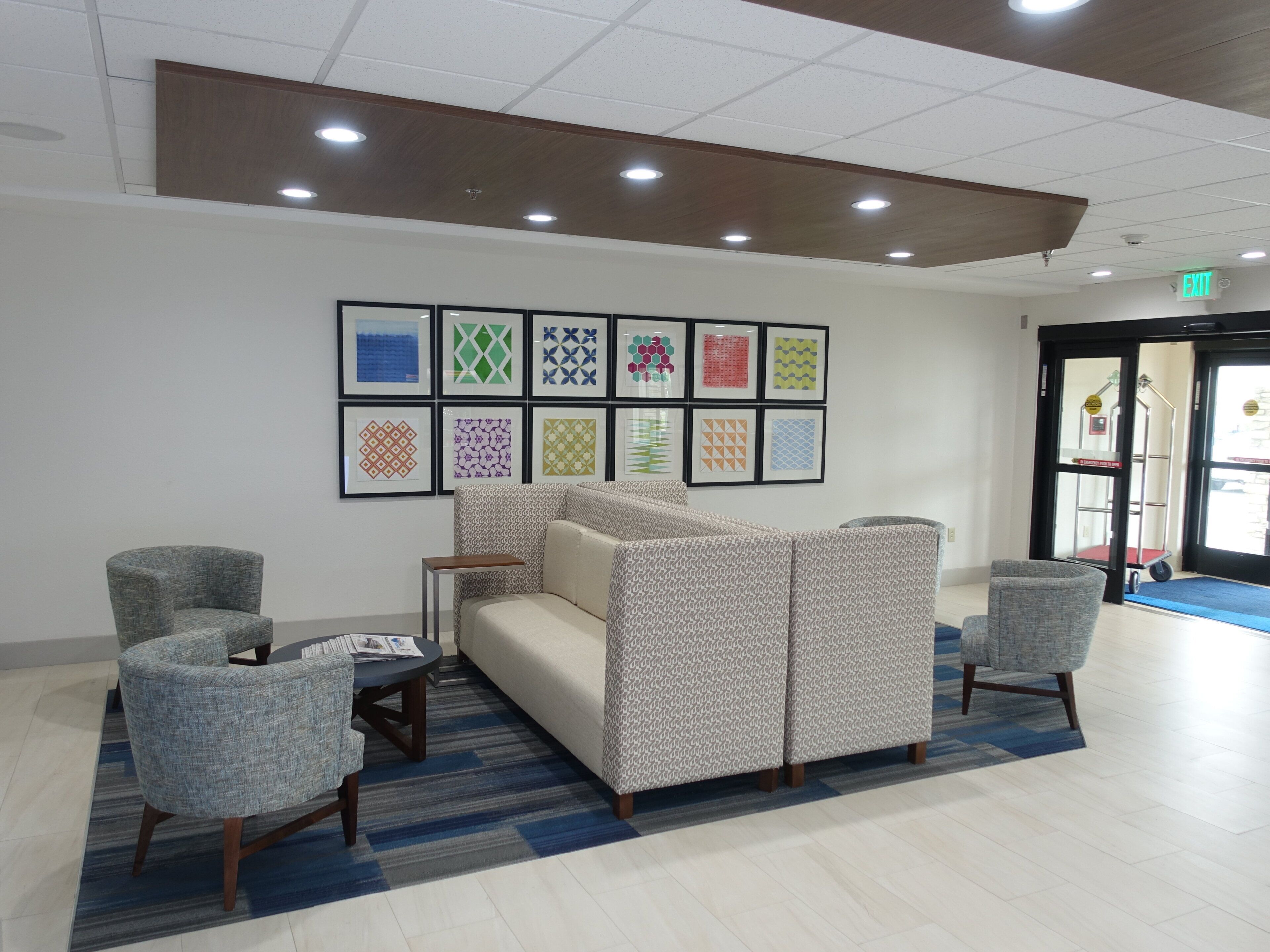 A lobby with a seating area, framed artwork on the wall, and an exit sign.