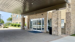 A building entrance with a covered walkway, stone facade, and a bench. - Holiday Inn Express & Suites La Porte by IHG (La Porte)