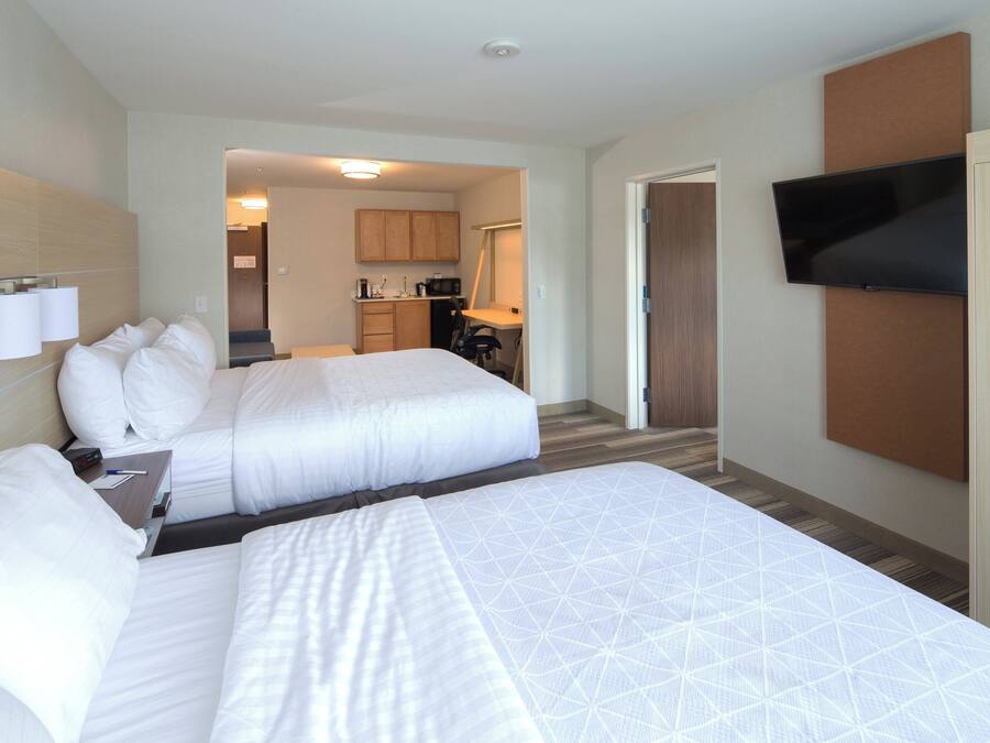 Habitación de hotel con dos camas, televisión, escritorio y kitchenette.