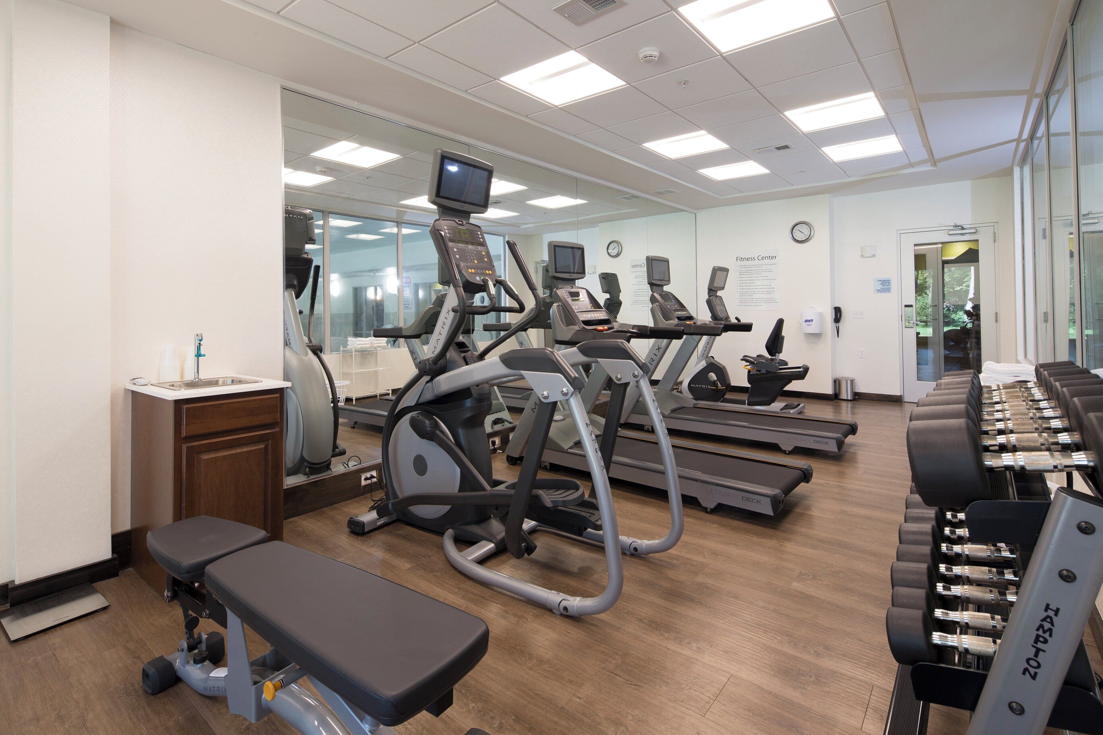 Un gimnasio con cintas de correr, elípticas y una banca.