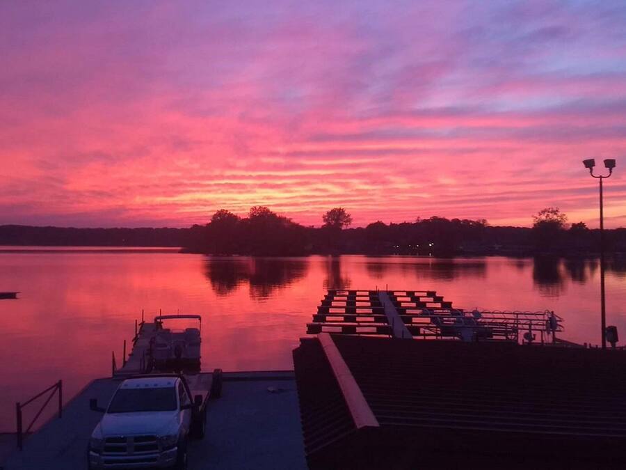 Un quai avec une voiture et un bateau, un lac paisible et un ciel au coucher du soleil.