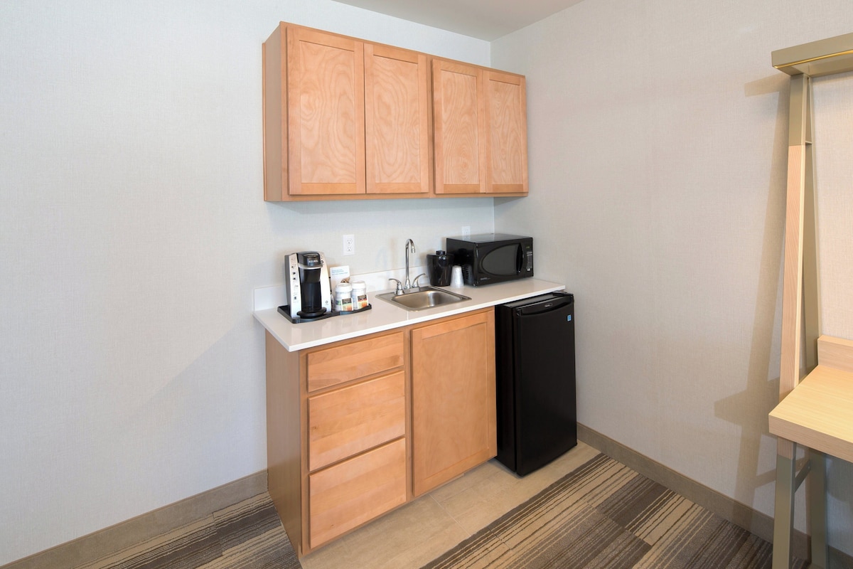 A compact kitchenette with wooden cabinets, a black refrigerator, a microwave, and a coffee maker.