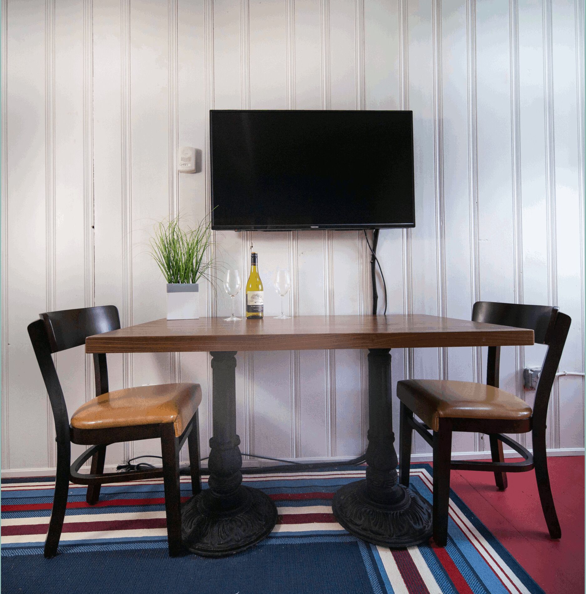 A dining area with a wooden table, two chairs, a potted plant, and a bottle of wine.