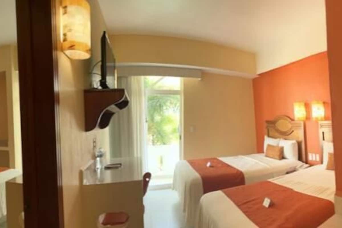 A hotel room with two beds, a bathroom, and a view of the outdoors.