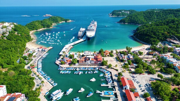 A coastal marina with multiple boats docked, a large cruise ship, and surrounding lush greenery. - Casa Danna Huatulco (Santa María Huatulco)