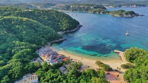 An aerial view of a coastal area with a beach, a small settlement with buildings, and a bridge in the distance. - Casa Danna Huatulco (Santa María Huatulco)