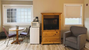 A compact living space with a wooden cabinet, a microwave, a small refrigerator, a television, a dining table with chairs, and a window with blinds. - Spruce Lane Lodge and Cottages (Lancaster)